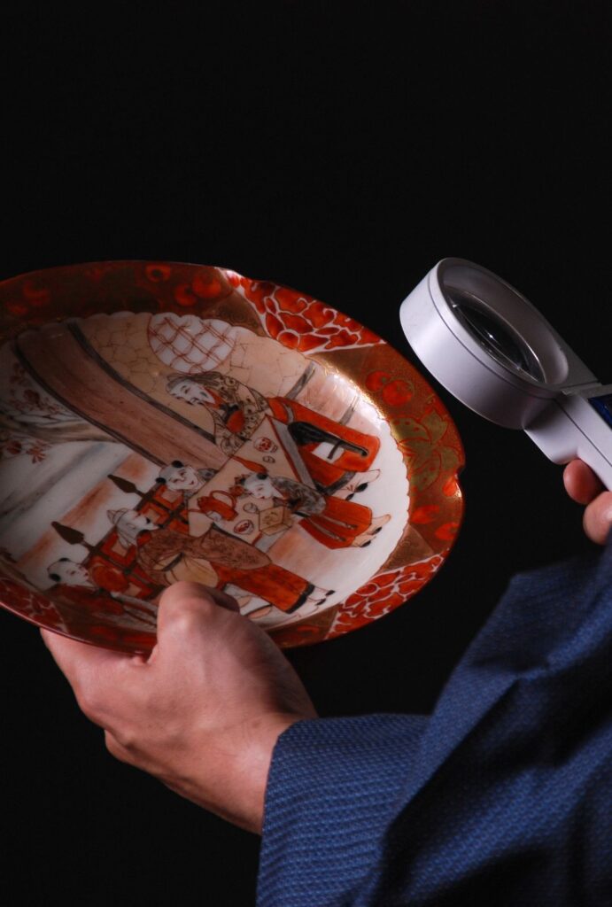 Person appraising an antique plate with a magnifying glass